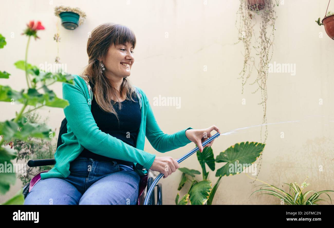 Junge Frau im Rollstuhl Bewässerung Pflanzen Stockfoto