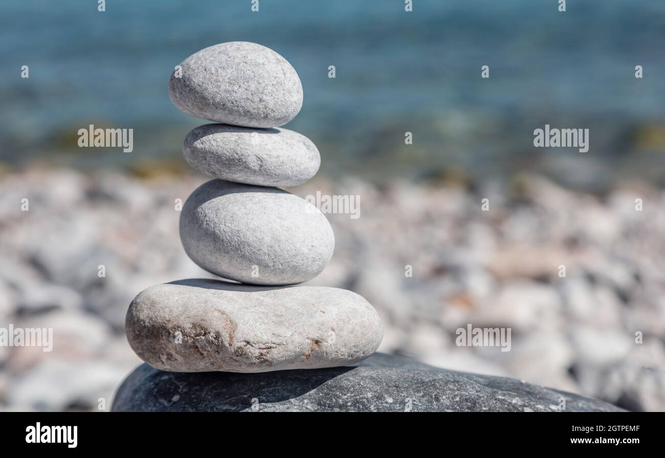 Balance, Zen-Steine, glatte Felspyramide auf Kiesstrand, blauer Meereshintergrund, sonniger Tag. Feng Shui, Harmonie und Frieden Konzept. Platz kopieren, te Stockfoto