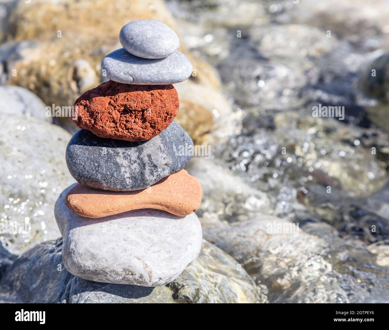 Zen-Balancesteine, glatter Felsturm auf nassem Kiesgrund gestapelt, sonniger Tag an der Küste. Harmonie und Frieden am Meer Stockfoto