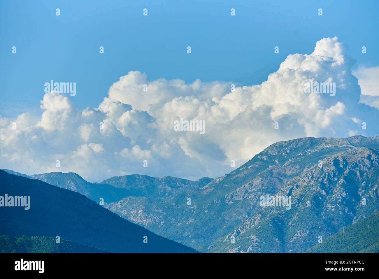 Flauschige Wolken über Berggipfeln in blauem Himmel und Wetterwechsel Stockfoto