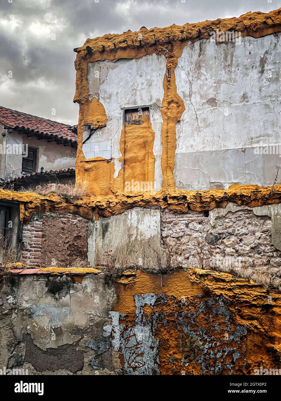 Ein Abriss eines alten Hauses in einem historischen Viertel, mit Wänden mit gelbem oder ockerem Polyurethanschaum und verfallenen Ziegelwänden, vertikal Stockfoto