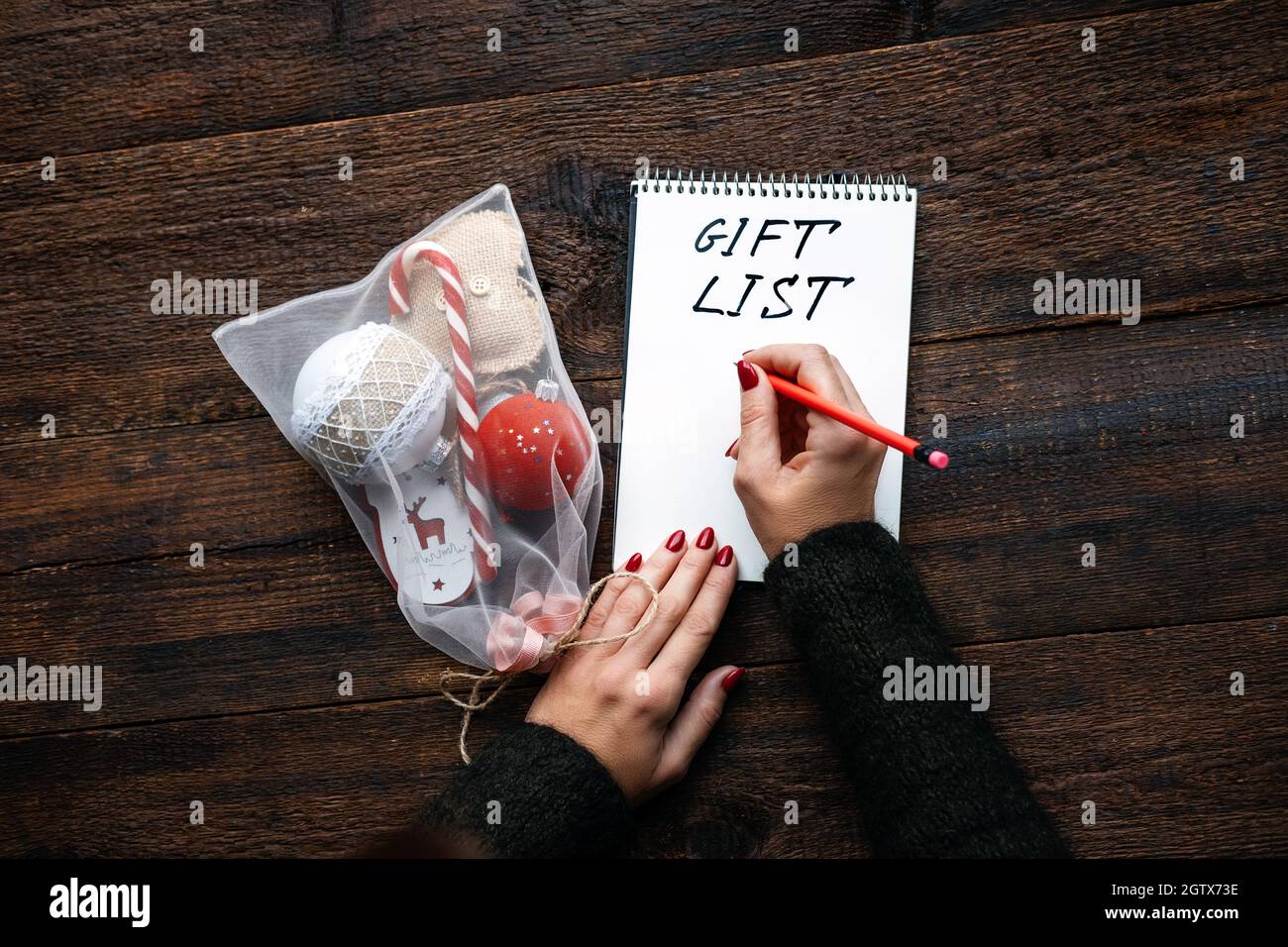 Weihnachtsgeschenk Liste, verfolgen Geschenke weihnachtszeit. Weibliche Hände mit offenem Notizblock und Text-Geschenkliste auf Holzhintergrund Stockfoto