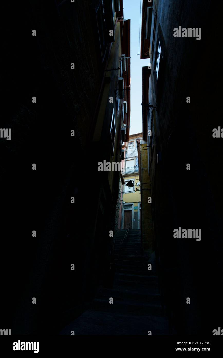 Dunkle Gasse zwischen bunten Gebäuden in Porto, Portugal. Typische traditionelle, farbenfrohe portugiesische Seitenstraße zwischen Gebäuden mit hohen Wohnungen. Stockfoto