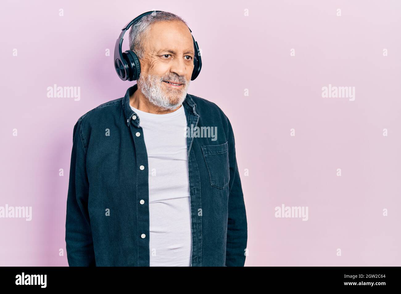 Gutaussehender älterer Mann mit Bart, der Musik hört, mit Kopfhörern