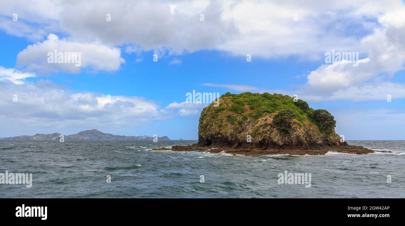 Eine kleine Insel weit vor der Küste mit dem Festland am Horizont sichtbar. Fotografiert in der Bay of Islands, Neuseeland Stockfoto