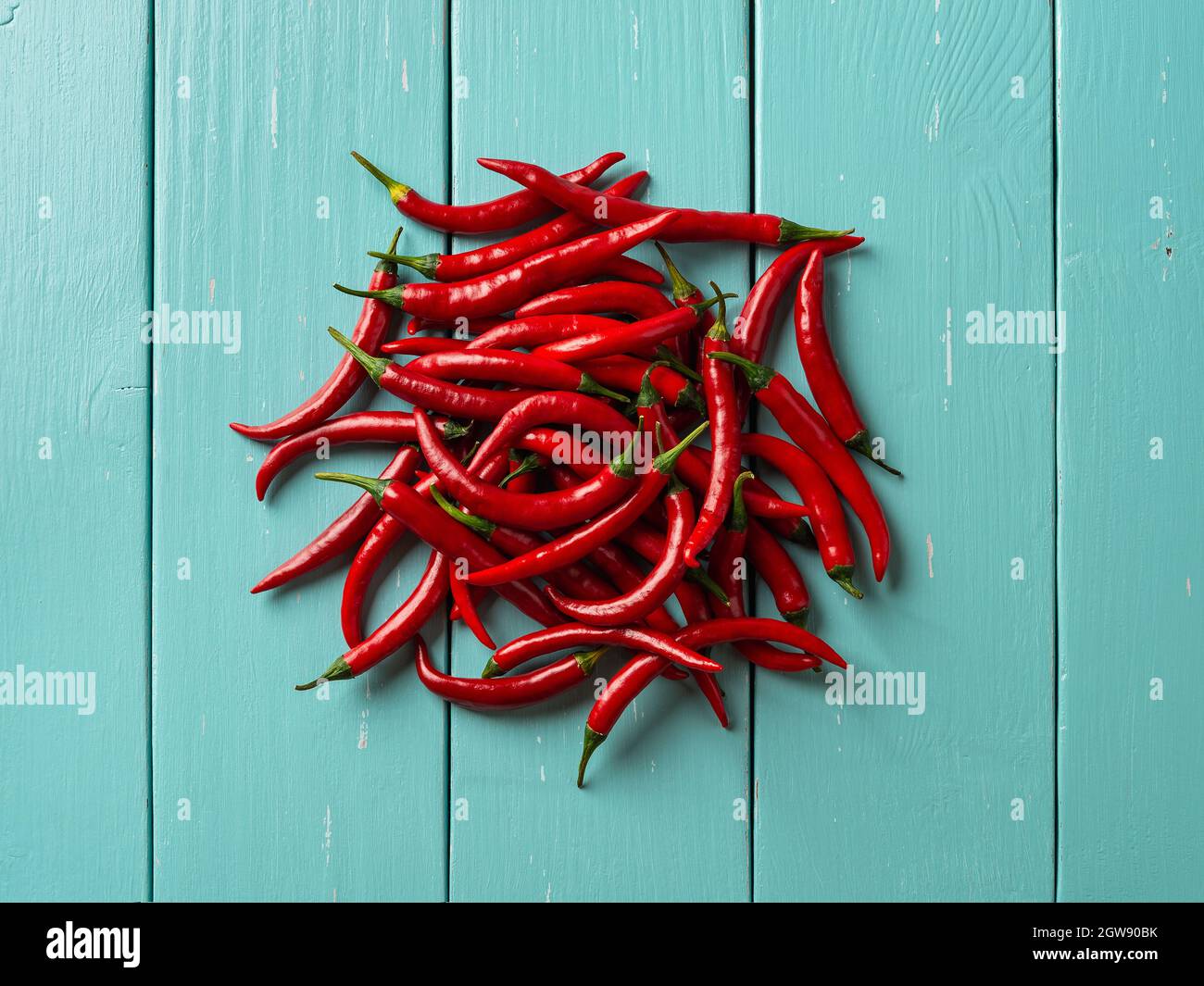 Ein paar rote, scharfe Chilischoten auf einem türkisfarbenen Holztisch. Ganze frische, scharfe Chilischoten auf der Tischplatte. Ein paar rohe Bio-Chilischoten aus der Draufsicht. Stockfoto