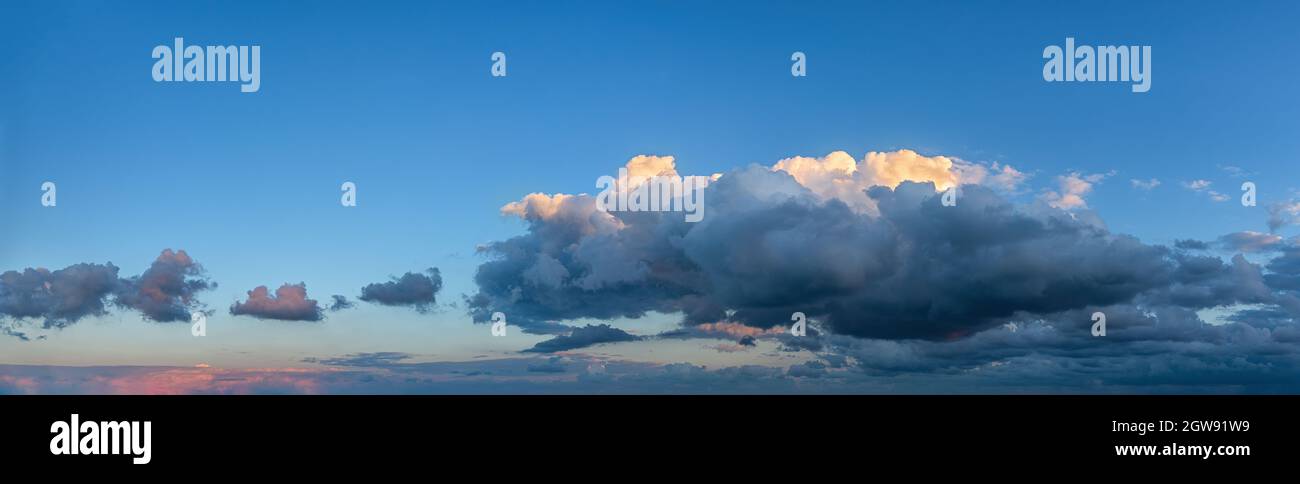Flauschige Kumuluswolken bewegen sich langsam tief über den Horizont im klaren blauen Himmel. Die Spitze der Wolke, die von der untergehenden Sonne beleuchtet wird, und der untere Teil ist dunkel. Stockfoto