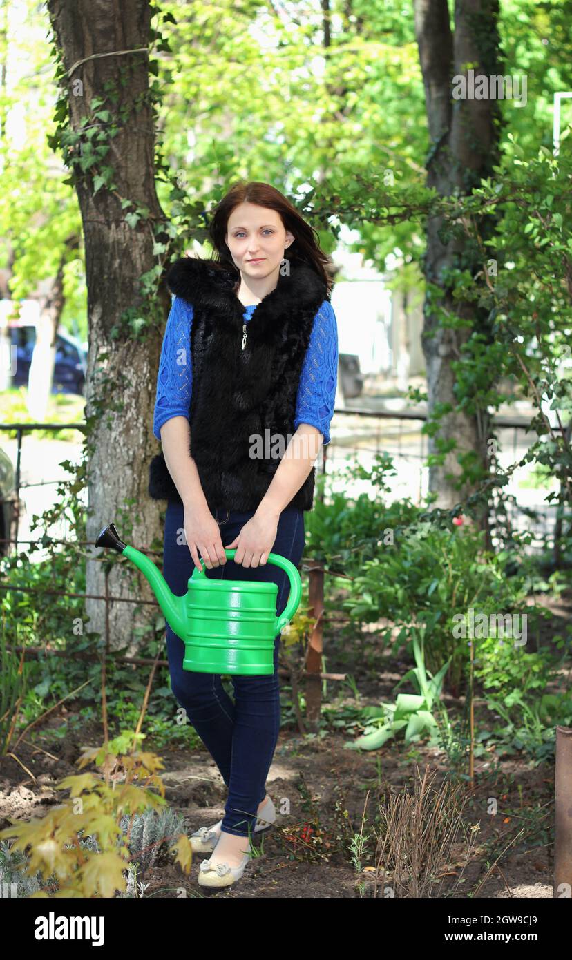 Junge positive Brünette Mädchen arbeitet in einem Frühlingsgarten, Pflanzen Bäume, Blasboden und Bewässerung Pflanzen Stockfoto