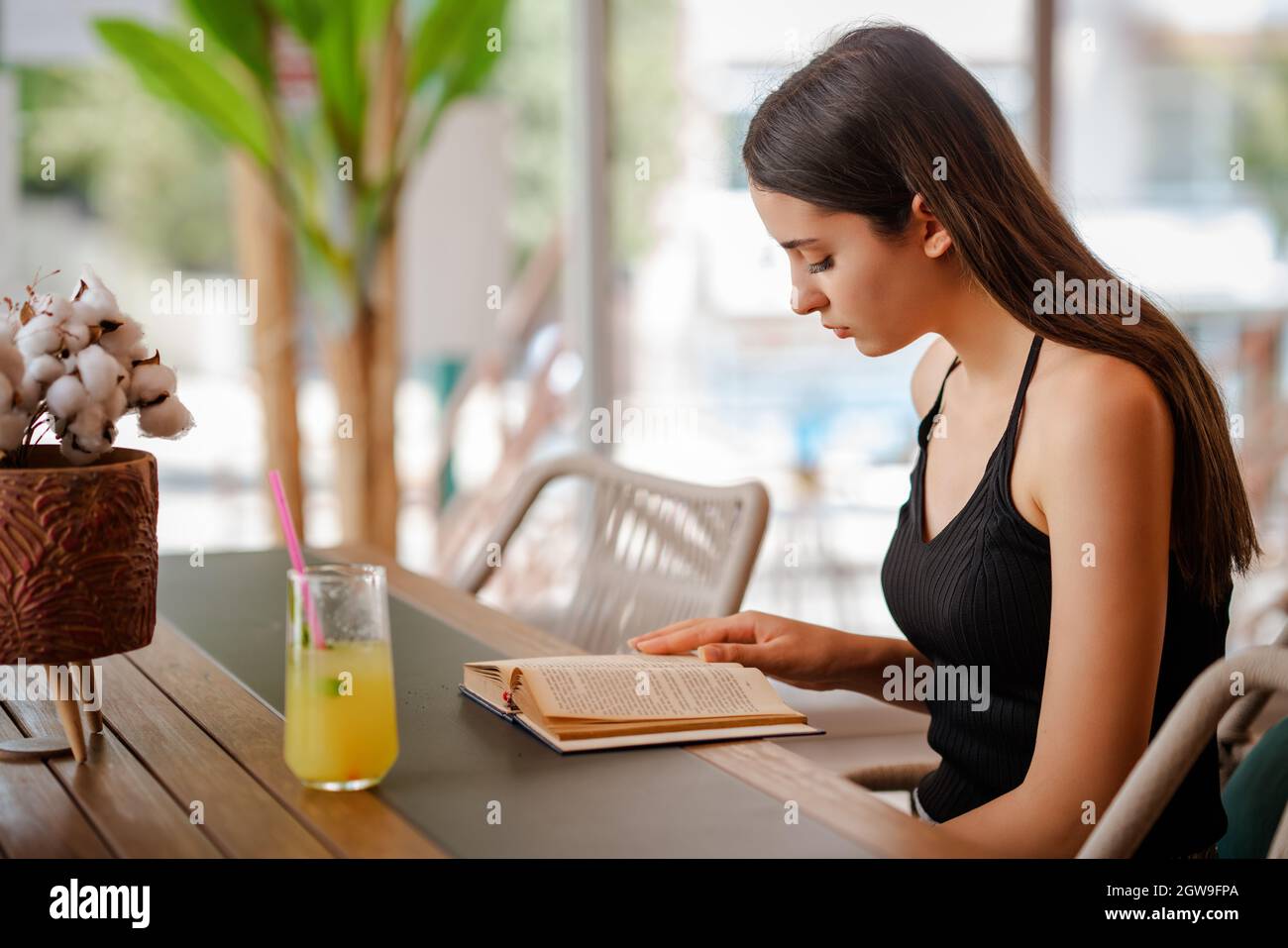 Junge hübsche Frau sitzt und trinkt eine Glaslimonade, während sie ein Buch liest. Hochwertige Fotos Stockfoto