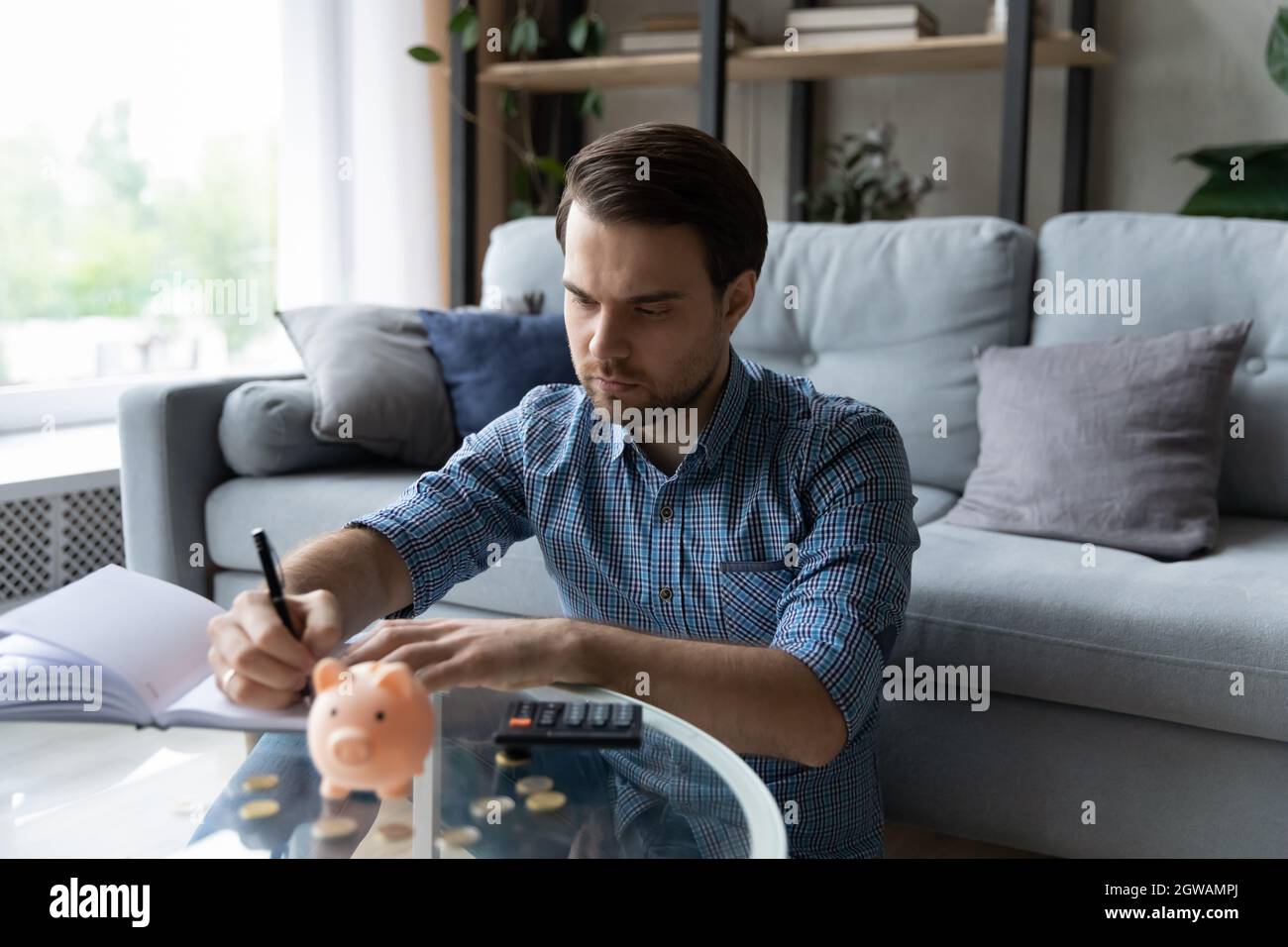 Serious Mann, der Finanzen verwaltet, sitzt am Tisch mit Sparschwein Stockfoto