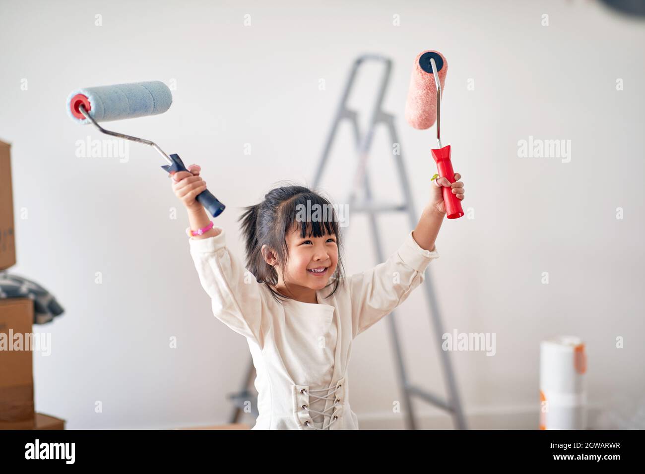Ein kleines Mädchen in fröhlicher Atmosphäre freut sich darauf, ein neues Zuhause zu malen, das sie gerade mit der Familie bezogen hat. Zuhause, Familie, Umzug Stockfoto