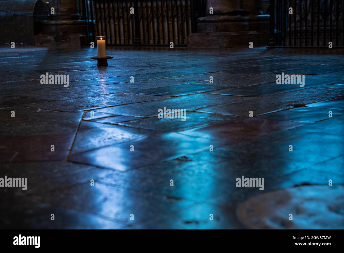 Einzelne Kerze leuchtet auf dem alten Steinboden in stimmungsvollem blauen Licht Stockfoto