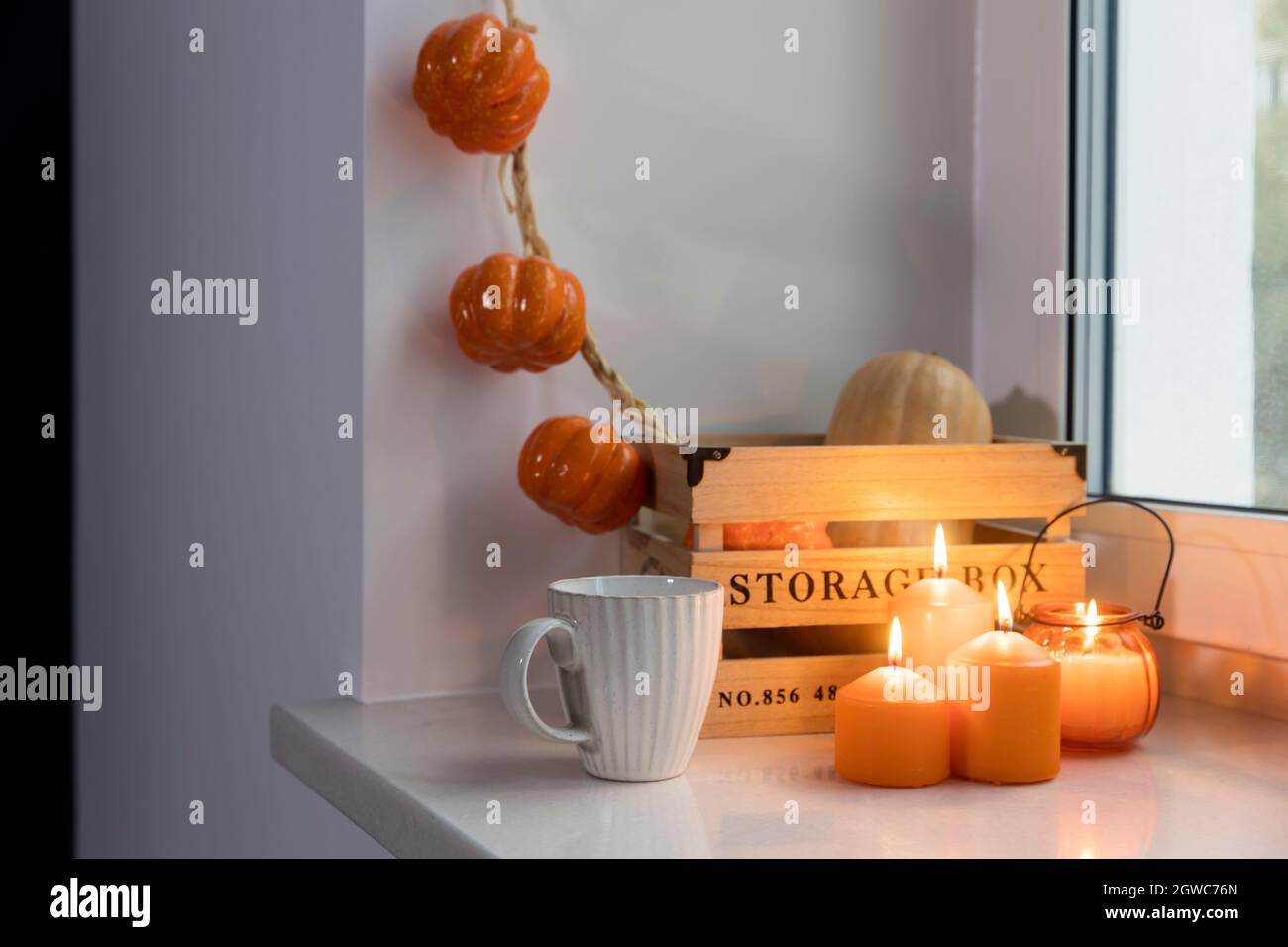 Dein Zuhause für Halloween vorbereiten. Eine hölzerne Kürbisdose, eine  falsche Kürbisgirlande, orangefarbene Kerzen, eine Tasse Tee und eine  Kerzenlaterne schmücken das Fenster Stockfotografie - Alamy