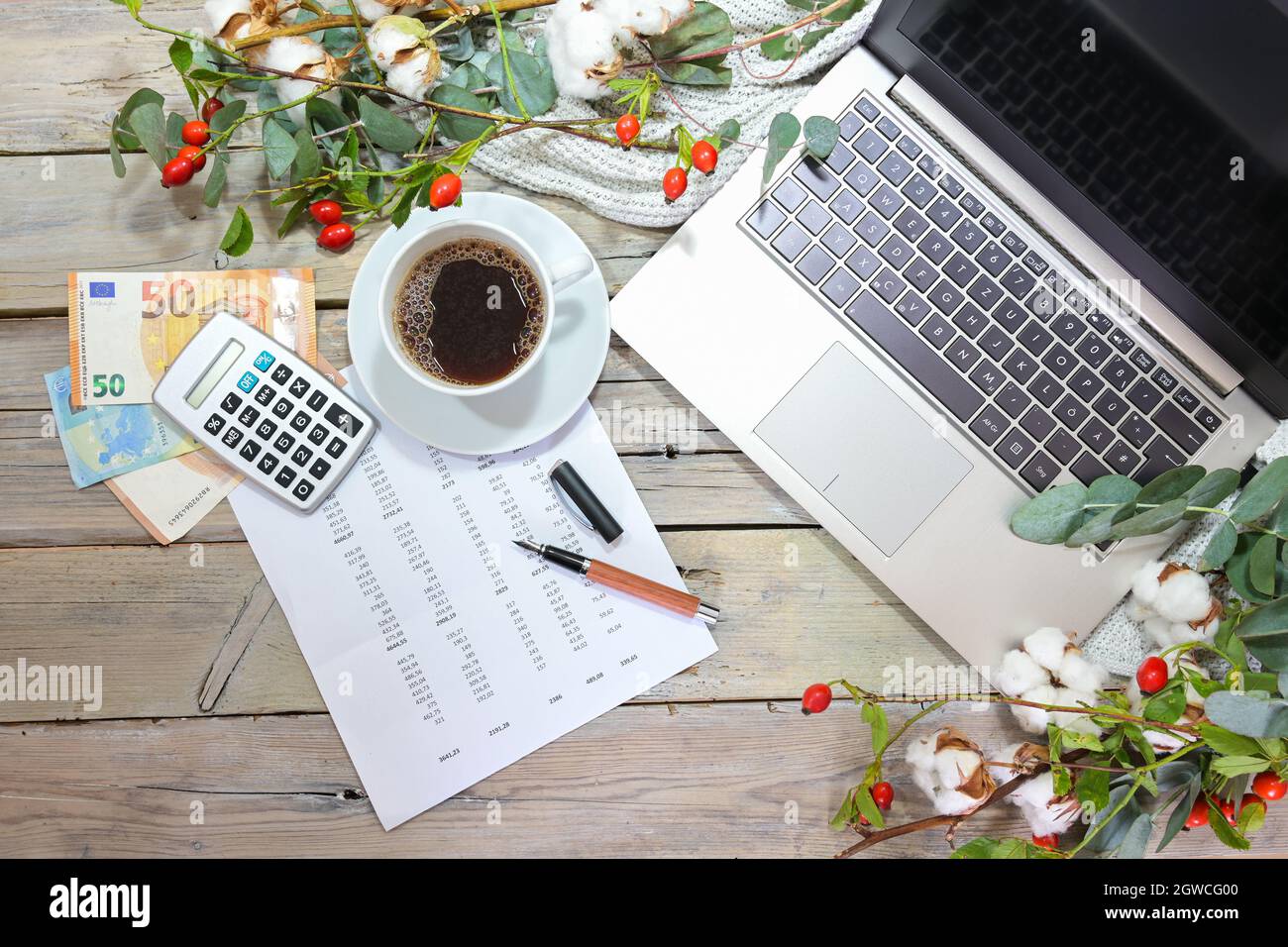 Laptop-Computer, Rechner, Geld und eine Kaffeetasse auf einem rustikalen Holztisch mit Herbstzweigen, saisonalen Geschäfts- und Finanzbuchhaltung im Hotel Stockfoto