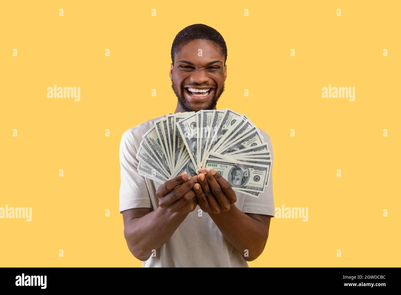 Riesiges Gewinnkonzept. Wohlhabender schwarzer Mann mit viel Geld begeistert über seinen großen Erfolg über gelben Studio-Hintergrund. Glücklicher junger Mann mit Dollar gewinnen Stockfoto