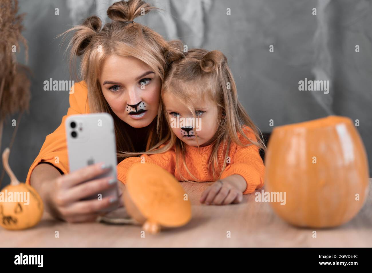 Mutter und Tochter spielen zu Hause zu Halloween ein Spiel am Telefon. Selfie von Hexen. Porträt von Frau und Mädchen mit Make-up und Smartphone Stockfoto
