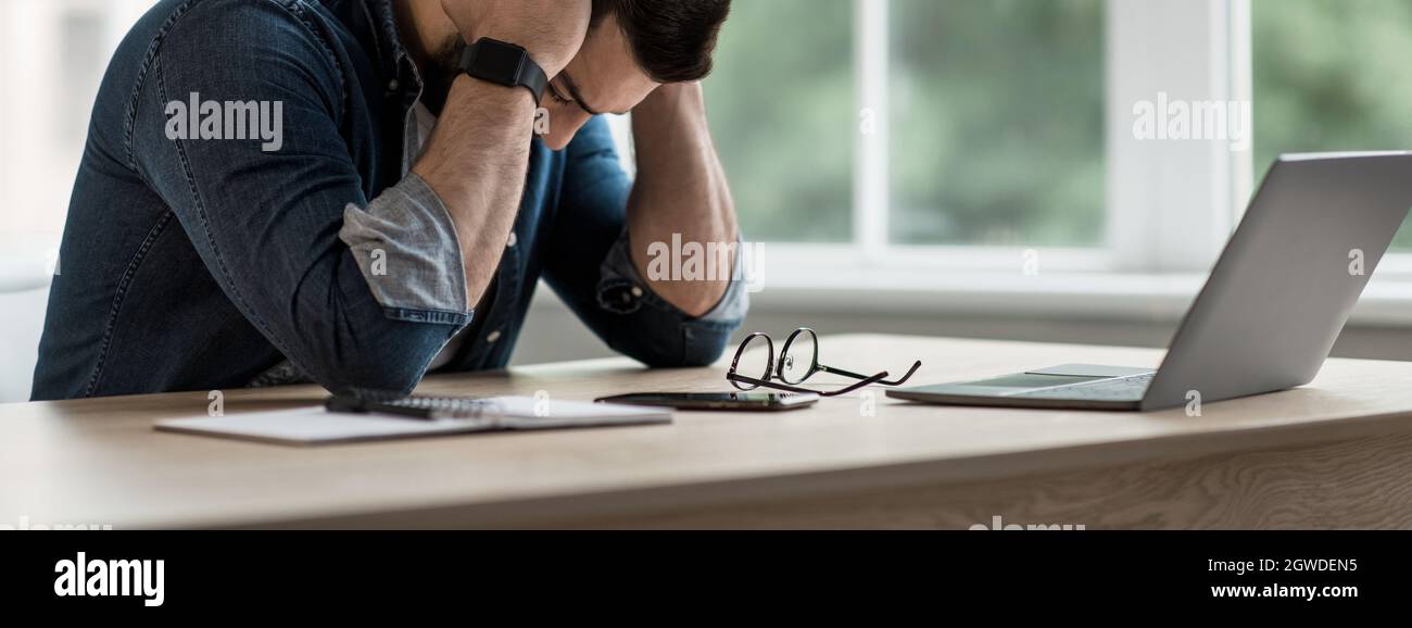 Deadline für Freiberufler. Müde unglücklicher junger Geschäftsmann, der den Kopf in den Händen hält, verärgert über Geschäftsversagen, Kopfschmerzen oder das Gefühl, über die Arbeit gestresst zu sein Stockfoto