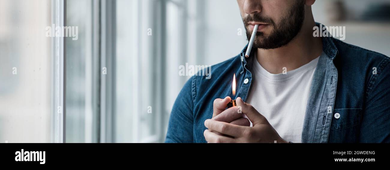 Junger Mann mit Zigarette in der Hand fühlt sich einsam und deprimiert. Nikotinabhängigkeit. Traurig unglücklich kaukasischen kaukasischen männlichen Beleuchtung Zigarette, auf groß Stockfoto