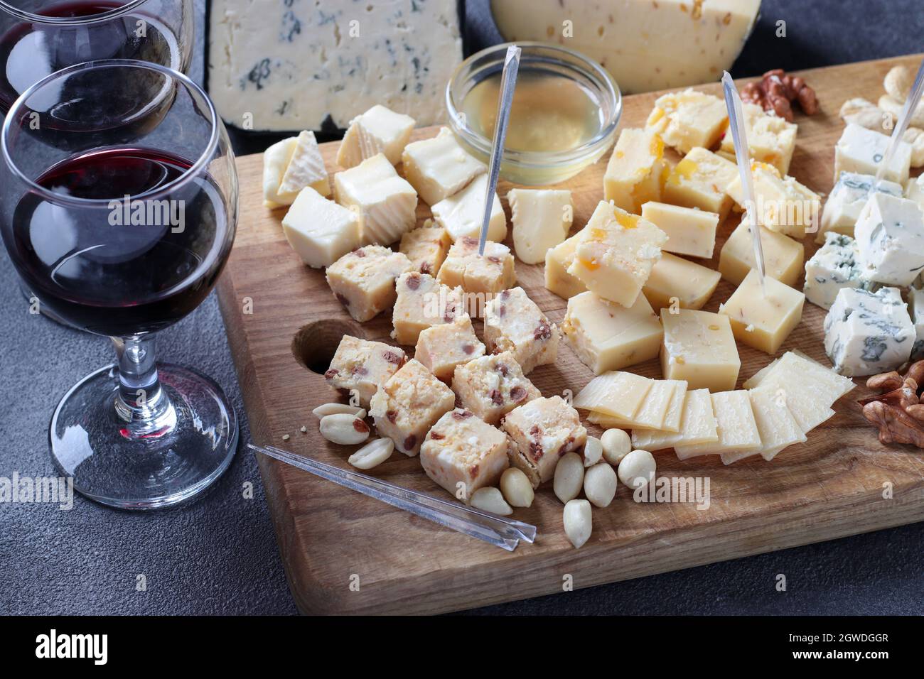 Spitzenkäse: Mit Trüffel, Dor blau, Brie, Parmesan und einer Auswahl von Nüssen auf einem Holzbrett auf dunkelgrauem Hintergrund. Weinparty-Snack. Stockfoto