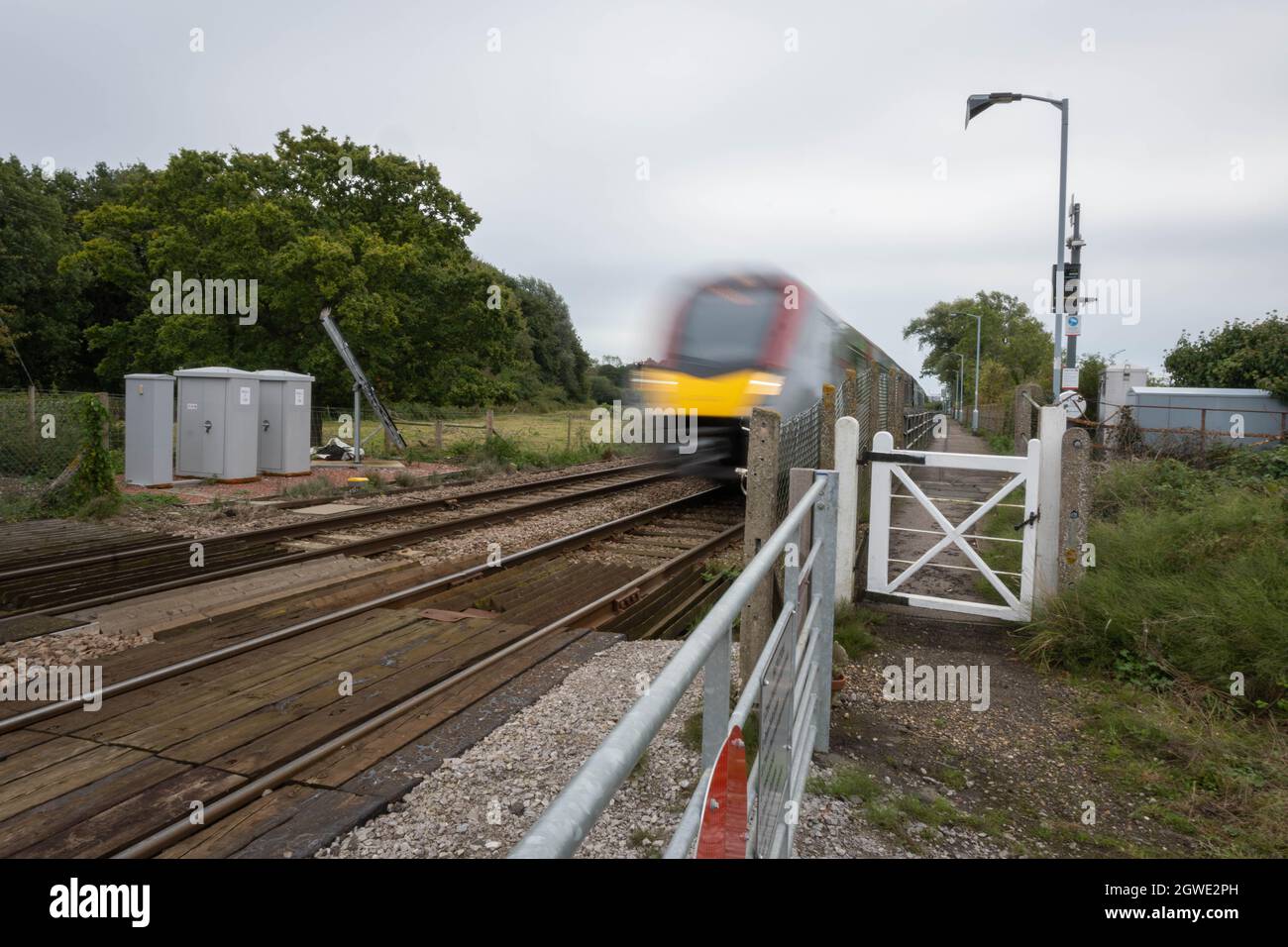 Unbemannte Bahnüberfahrt am Bahnhof Buckenham mit einem Zug der British Rail-Klasse 755, der mit hoher Geschwindigkeit in Richtung Bahnhof Norwich fährt. Stockfoto