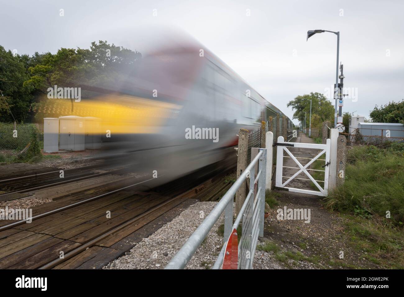 Unbemannte Bahnüberfahrt am Bahnhof Buckenham mit einem Zug der British Rail Klasse 755, der mit hoher Geschwindigkeit in Richtung Norwich Station fährt. Stockfoto