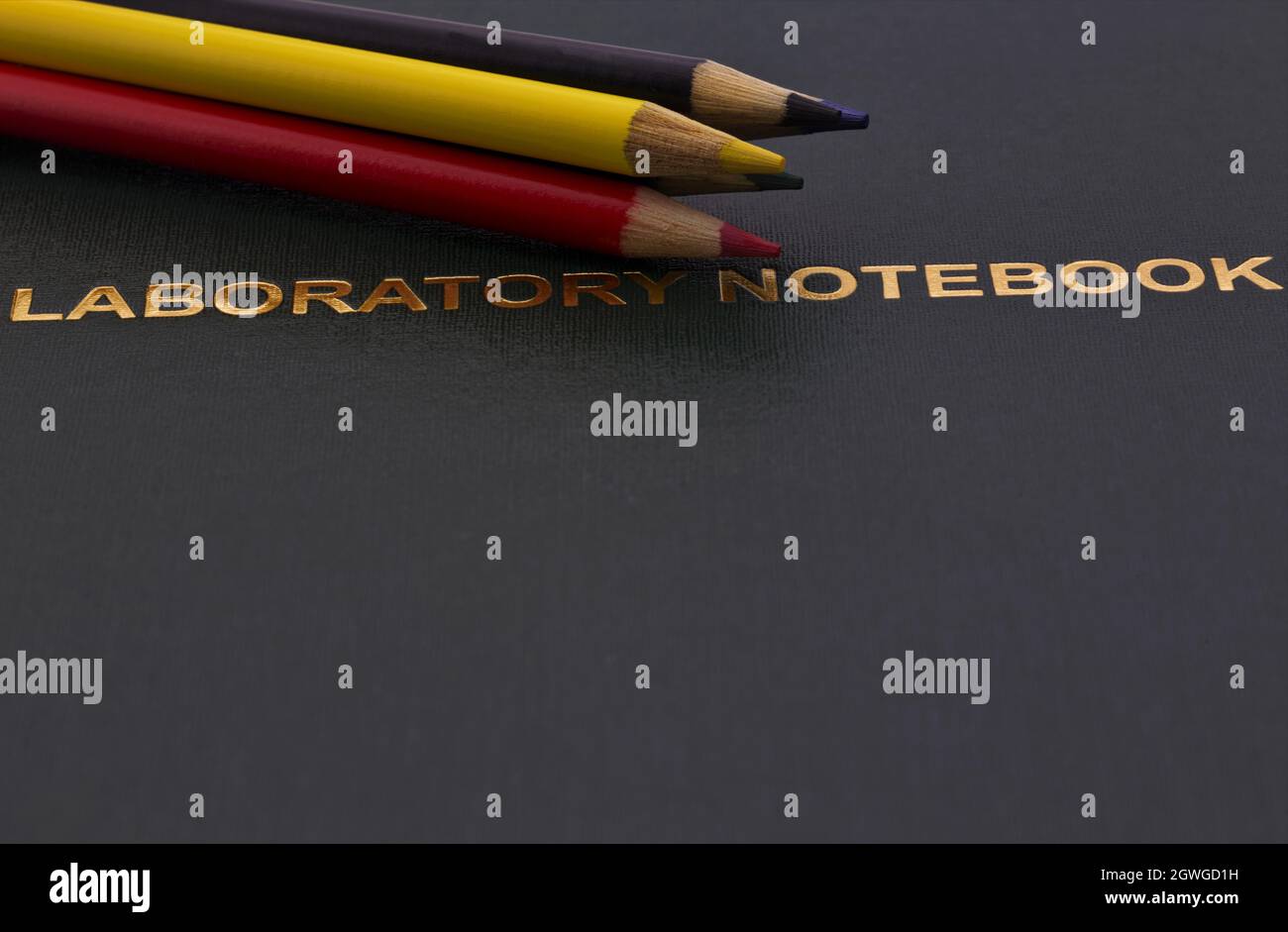 Buntstifte, die auf goldfarbenen, dunklen wissenschaftlichen Labornotizbüchern angebracht sind, spiegeln die Betonung von Universität, Forschung und Bildung auf sorgfältiger Notatio wider Stockfoto