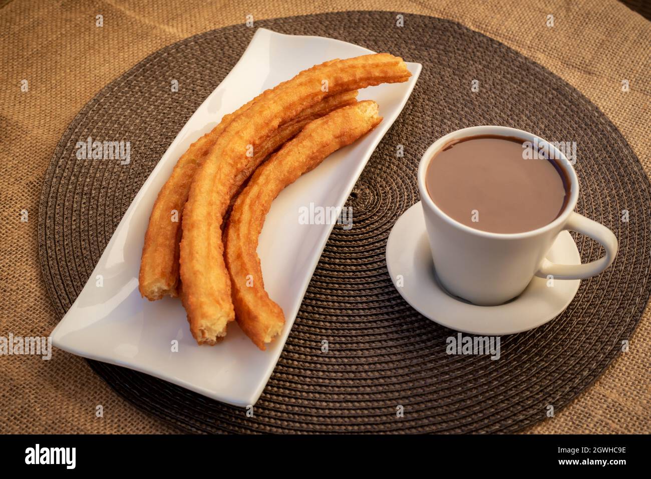 Teller mit Churros neben einer Tasse Schokolade auf einer karierten Tischdecke. Stockfoto