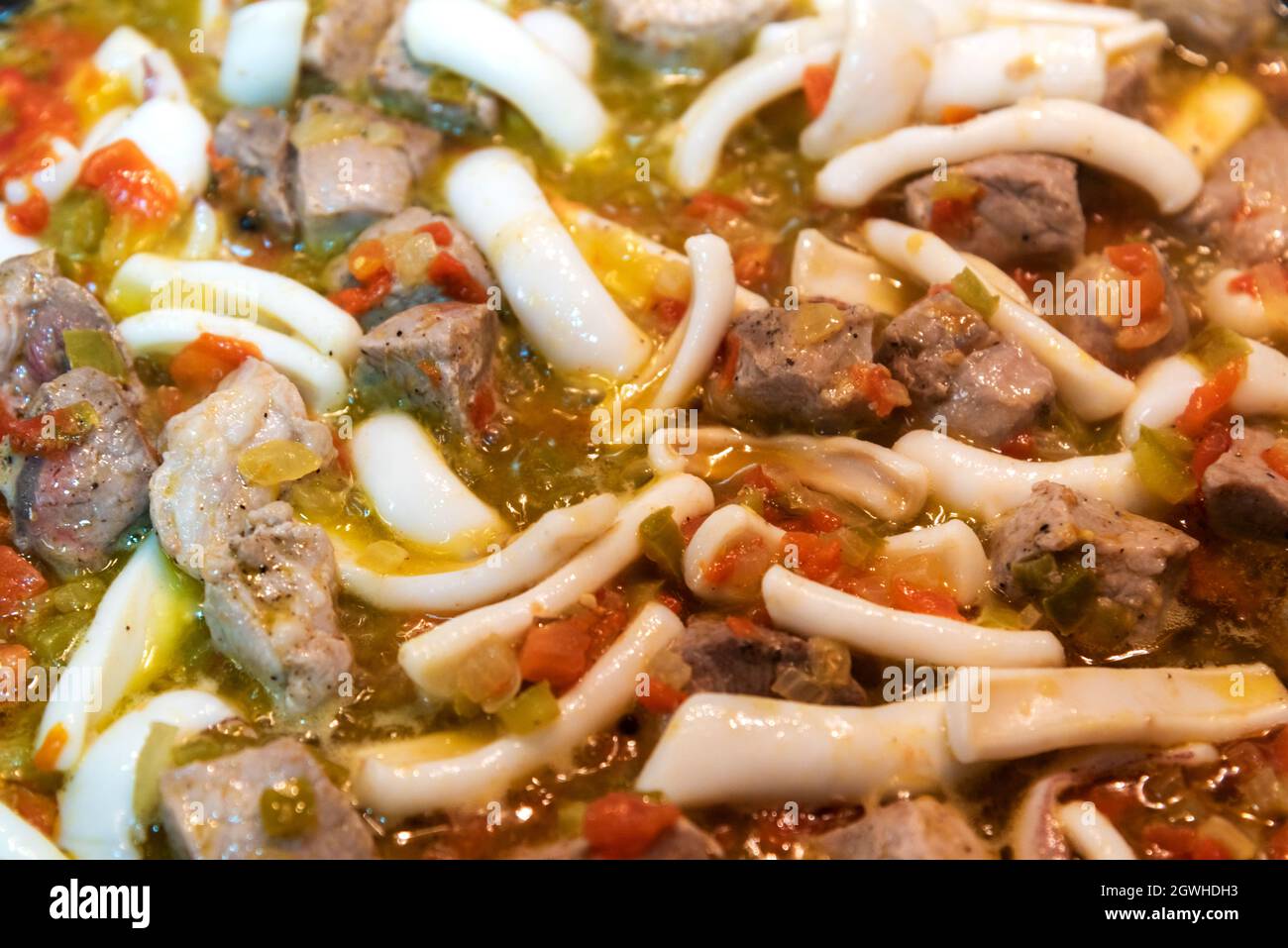Tintenfisch und Schweinefleisch in einer Pfanne auf dem Feuer neben dem gebratenen Gemüse Stockfoto