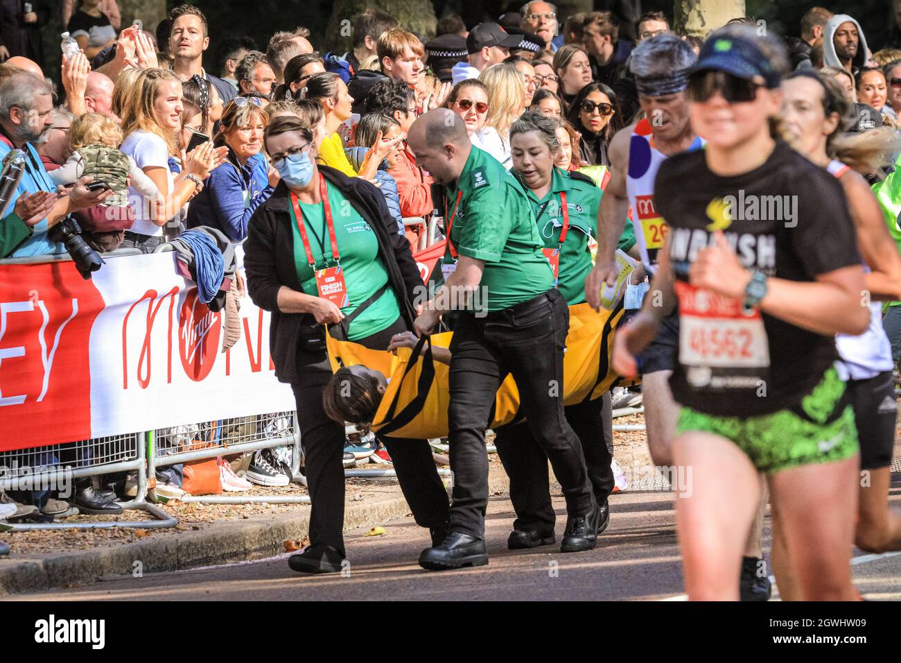 London, Großbritannien. Oktober 2021. Einem eingestürzten Läufer wird auf der letzten Meile beim Birdcage Walk von Sanitätern geholfen. Nach einer 2-jährigen Abwesenheit kehrt der Virgin Money London Marathon zu seinem traditionellen Kurs von Blackheath zur Mall zurück. Mit über 40,000 Teilnehmern und einer ähnlichen Zahl, die gleichzeitig den virtuellen Marathon auf einer Strecke ihrer Wahl absolvieren wird es der größte Marathon überhaupt sein. Kredit: Imageplotter/Alamy Live Nachrichten Stockfoto
