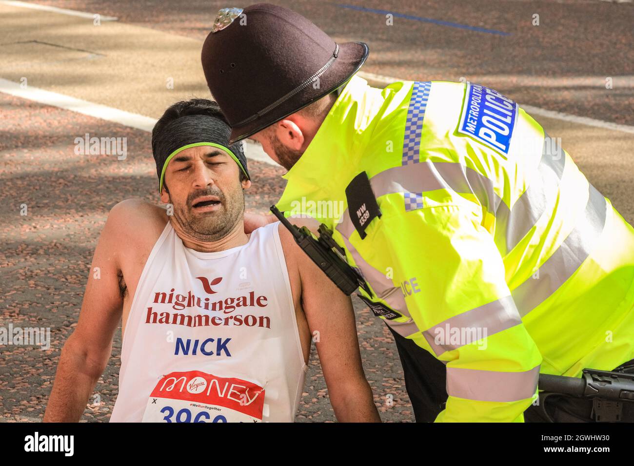 London, Großbritannien. Oktober 2021. Auf der letzten Meile beim Birdcage Walk wird einem eingestürzten Läufer von Polizei und Sanitätern geholfen. Nach einer 2-jährigen Abwesenheit kehrt der Virgin Money London Marathon zu seinem traditionellen Kurs von Blackheath zur Mall zurück. Mit über 40,000 Teilnehmern und einer ähnlichen Zahl, die gleichzeitig den virtuellen Marathon auf einer Strecke ihrer Wahl absolvieren wird es der größte Marathon überhaupt sein. Kredit: Imageplotter/Alamy Live Nachrichten Stockfoto