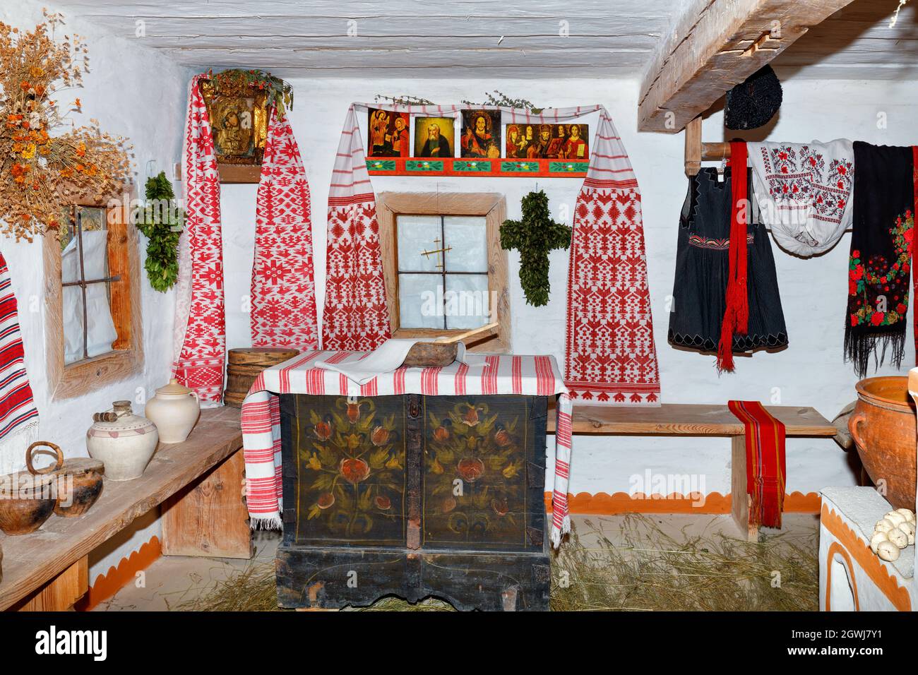 Das Innere der Wohnräume einer antiken ukrainischen ländlichen Hütte mit heiligen Bildern über dem Fenster und alten Kleidern und Geschirr. Stockfoto