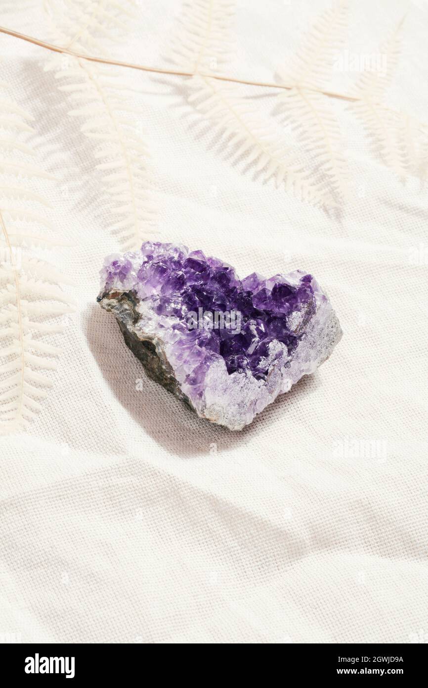 druse roher purpurner Amethyst-Kristall auf Stein auf grauem Leinen mit Farn, magischer Fels für Ritual, Hexerei, spirituelle Praxis, Meditation Stockfoto