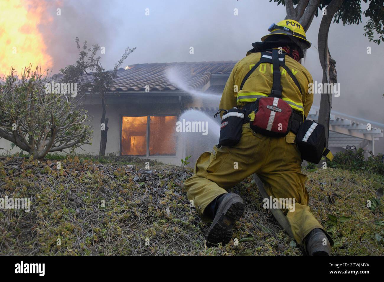 Der Feuerwehrmann von Poway leitet den Schlauchstrom während des Witch Creek Fire, 2007, in Richtung der Struktur. Die Struktur entzündete sich aufgrund brennender Glut, die unter dem Dach von Eben lag. Stockfoto