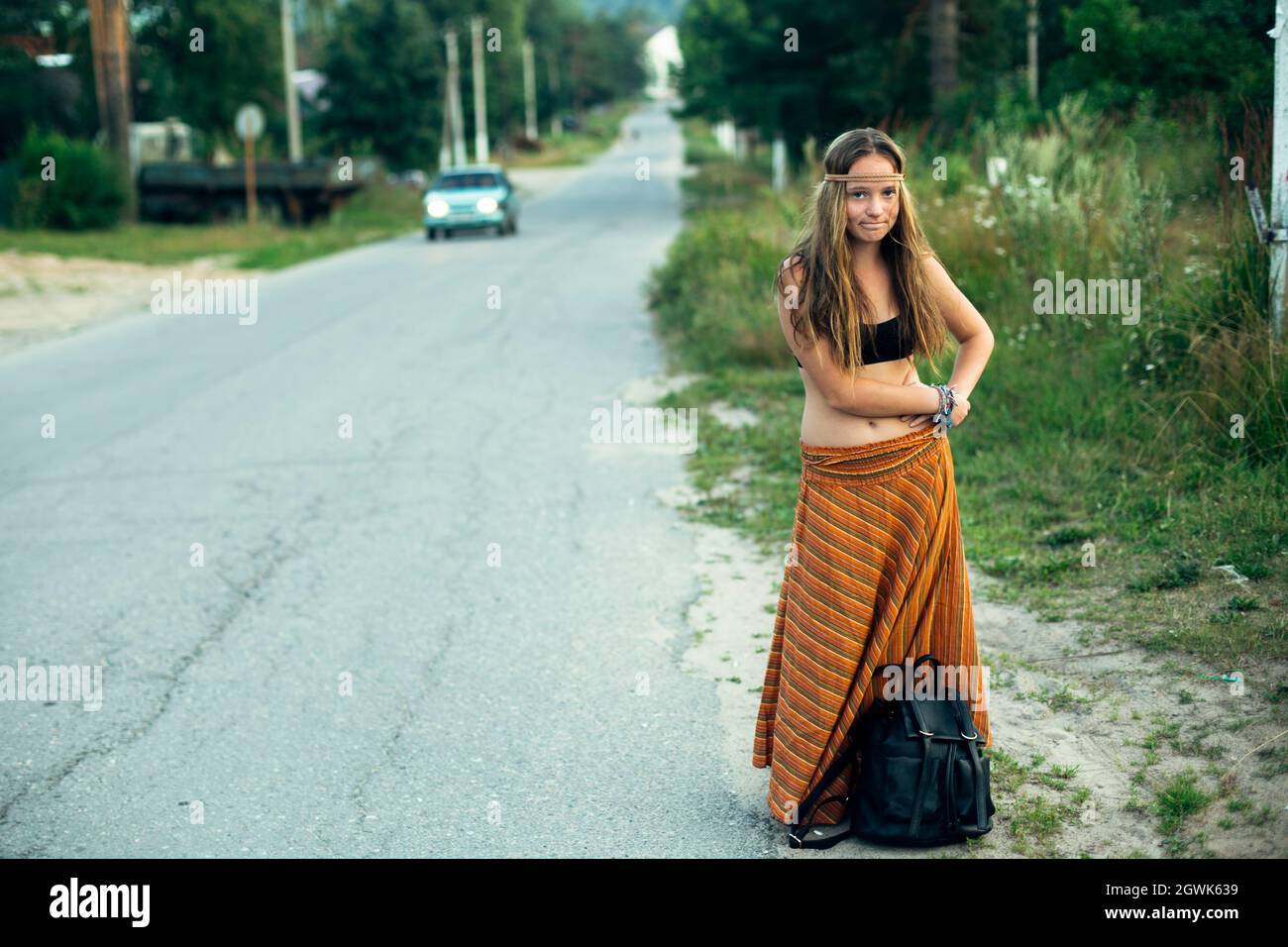 Ein Hippie-Mädchen, das in der Nähe der Straße stimmt. Anhalter für Wanderungen. Stockfoto