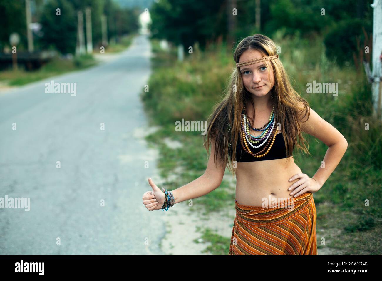 Ein Hippie-Mädchen steht bei der Abstimmung in der Nähe der Straße. Anhalter für Wanderungen. Stockfoto