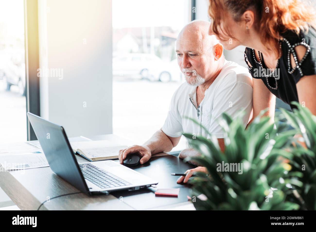 Geschäftsmann mittleren Alters im Büro. Assistent steht neben ihm und bekommt Anweisungen. Geschäftskonzept. Stockfoto