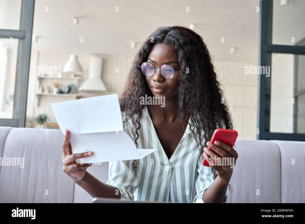 Junge ernsthafte afroamerikanische Geschäftsfrau liest Brief mit Handy. Stockfoto