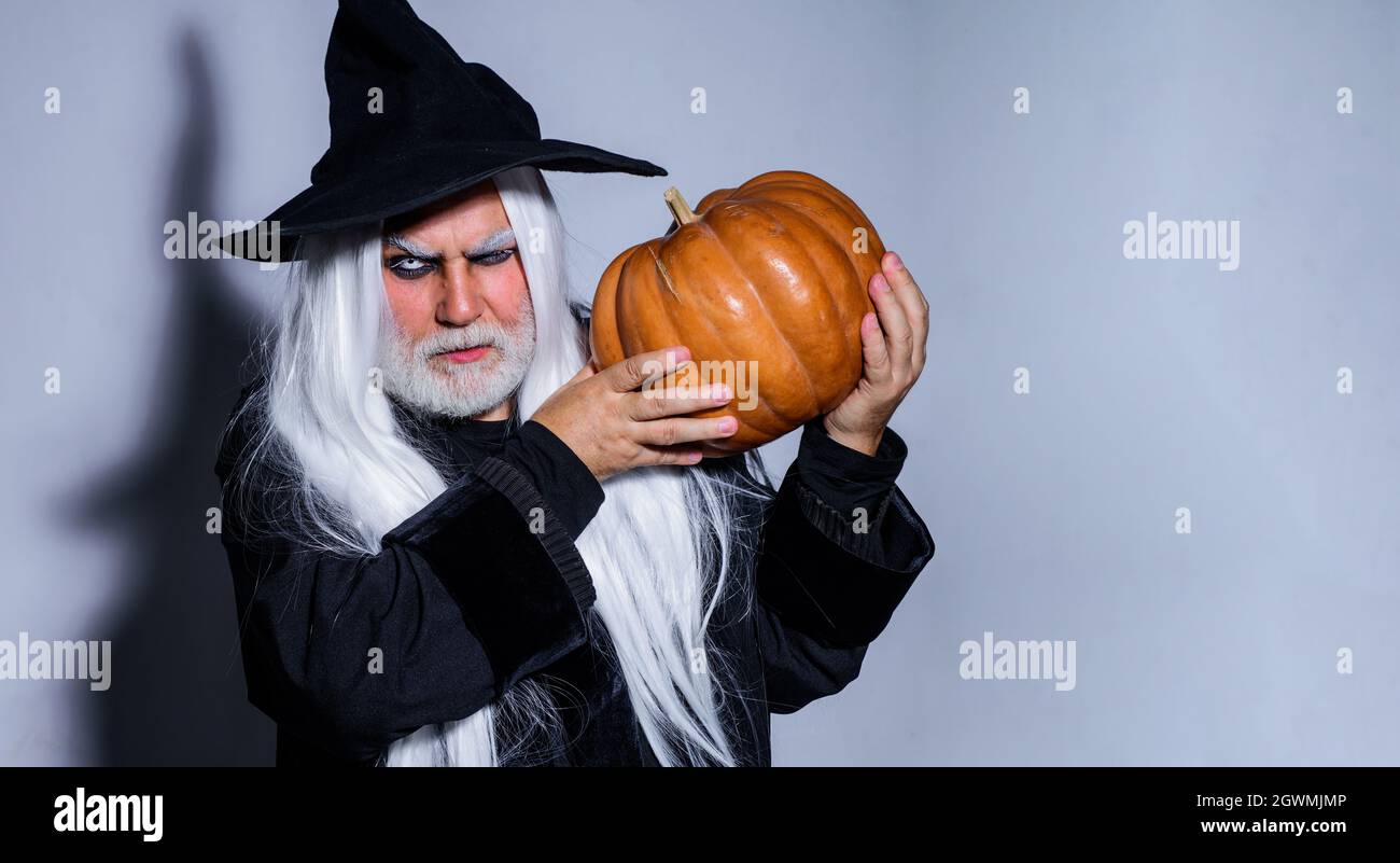 Schöner Mann im Hexenkostüm mit Kürbis in der Hand bereit zur Halloween-Party. Teufelsmann. Zauberhut. Stockfoto