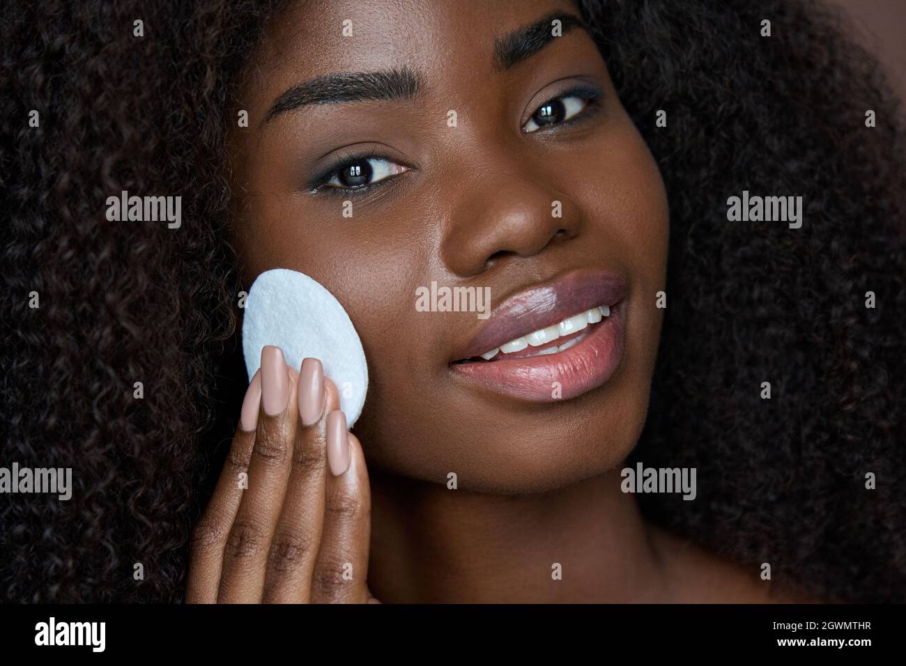 Schwarze junge Frau hält Wattepad entfernen Gesicht Make-up mit Make-up-Entferner. Stockfoto
