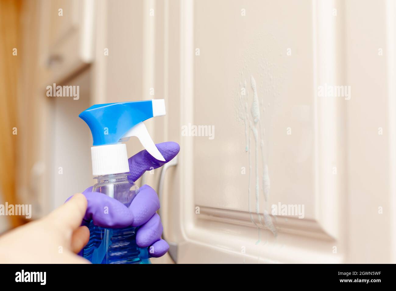 Waschmittel aus einer Sprühflasche sprüht auf die Tür des Küchenschranks Stockfoto