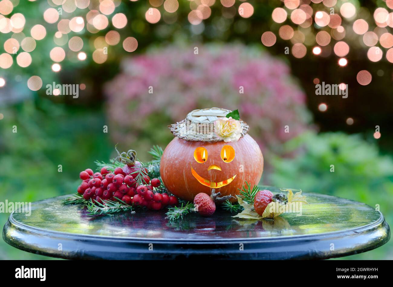 Auf einem Gartentisch sitzt ein witziger Halloween-Kürbis mit leuchtenden Augen und einem toothy Lächeln. Selektiver Fokus Stockfoto