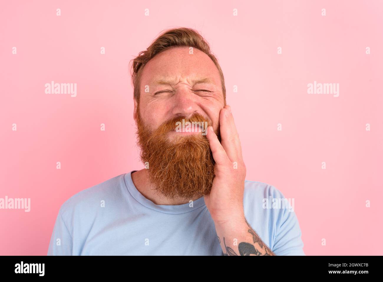 Glücklicher Mann mit hellblauem T-Shirt hat Schmerzen in den Zähnen Stockfoto