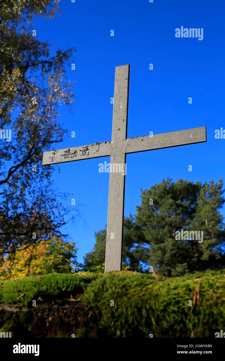 Altes metallisches Kreuz gegen blauen Himmel, mit herbstlichen Bäumen im Hintergrund. Stockfoto