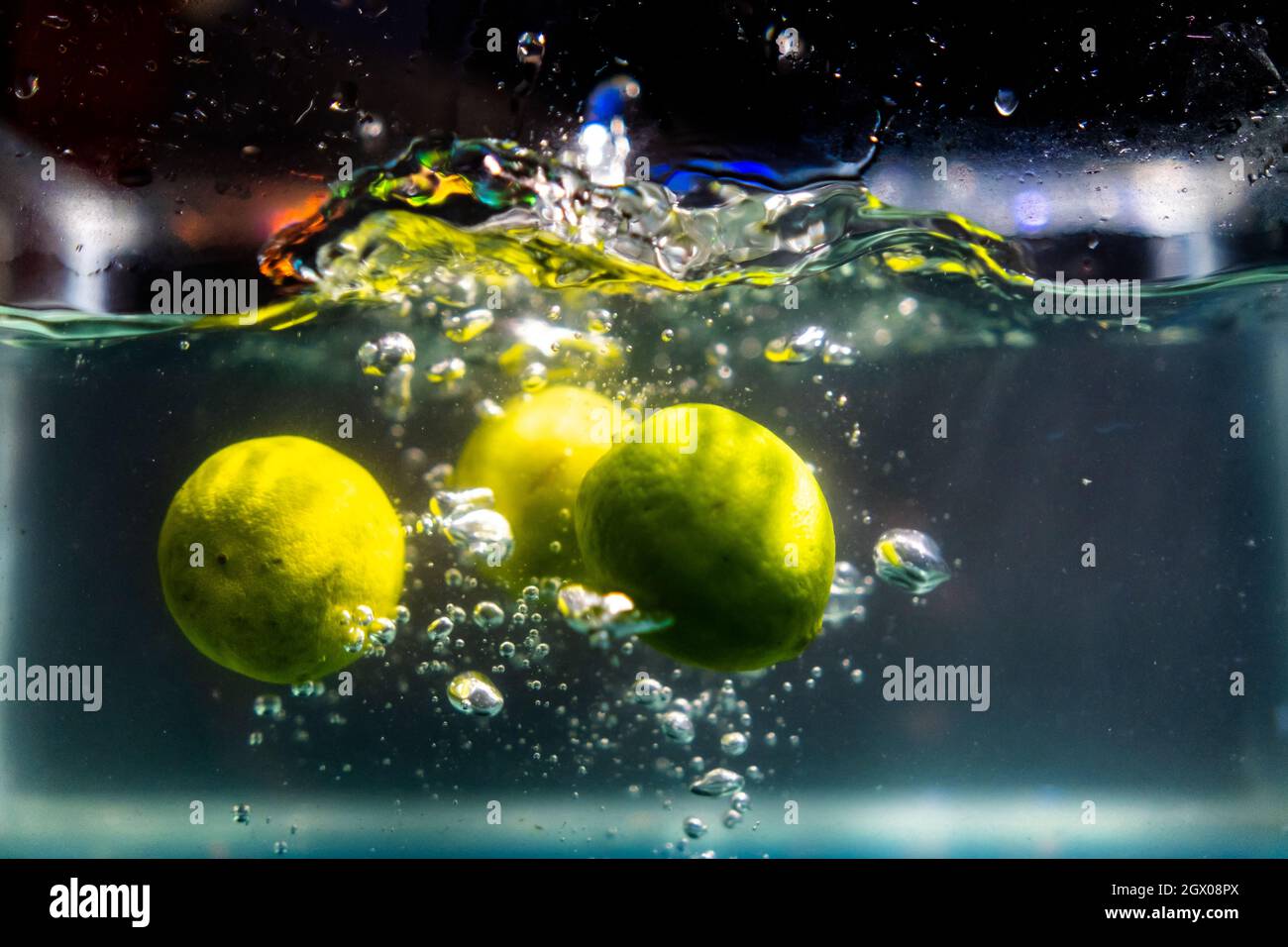 Drei frische Limetten, die mit Spritzern tief ins Wasser fallen Stockfoto