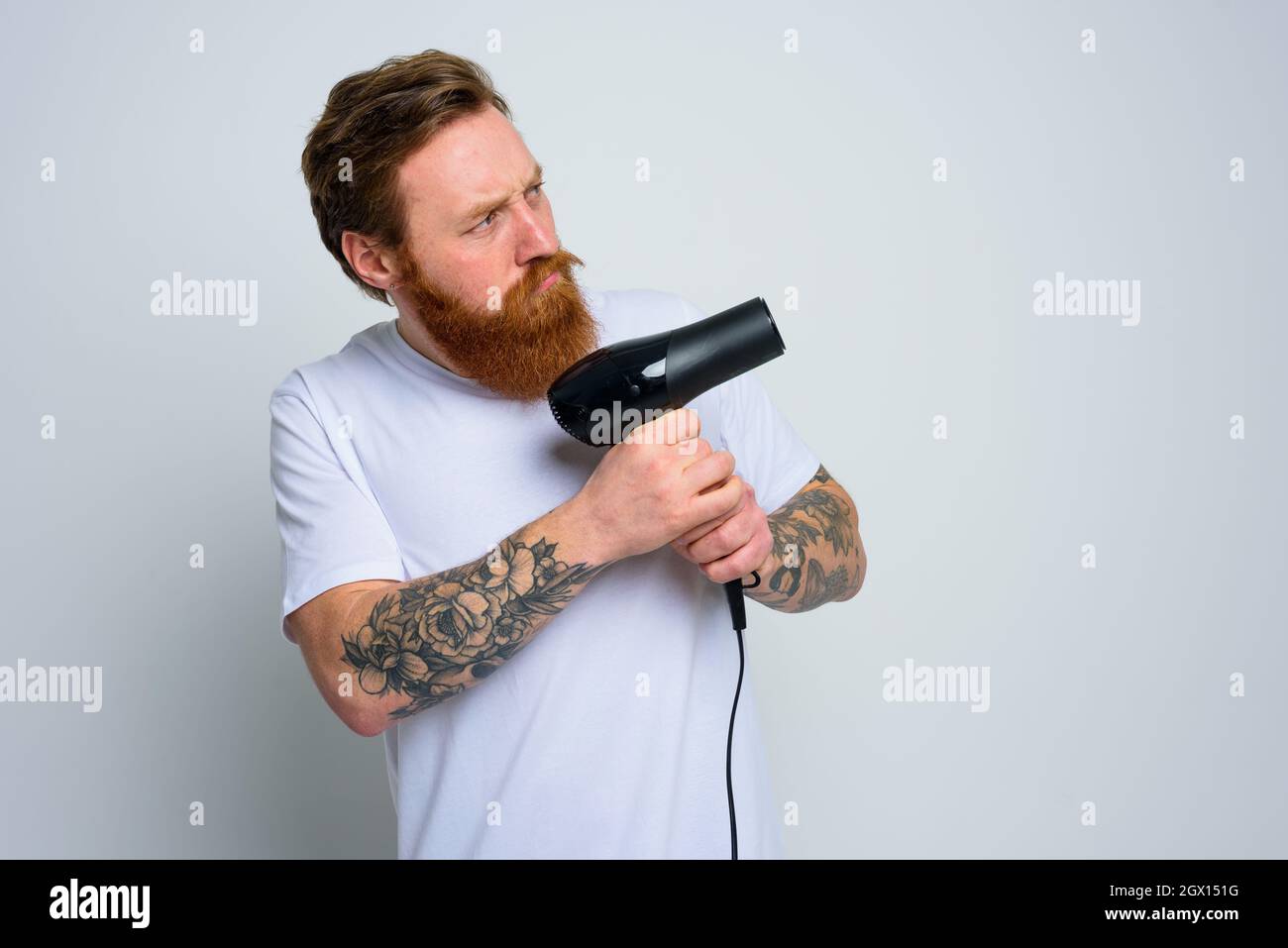 Serious Mann mit Bart spielen mit Haar dryeras eine Pistole Stockfoto