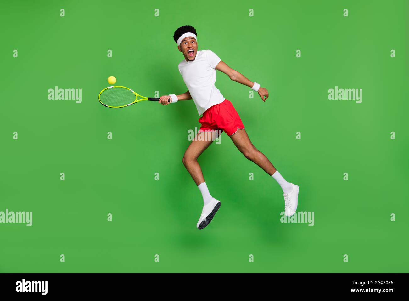 In voller Länge Foto von ziemlich schockiert dunkle Haut Kerl gekleidet Sport-Outfit spielen Tennis springen isoliert grüne Farbe Hintergrund Stockfoto