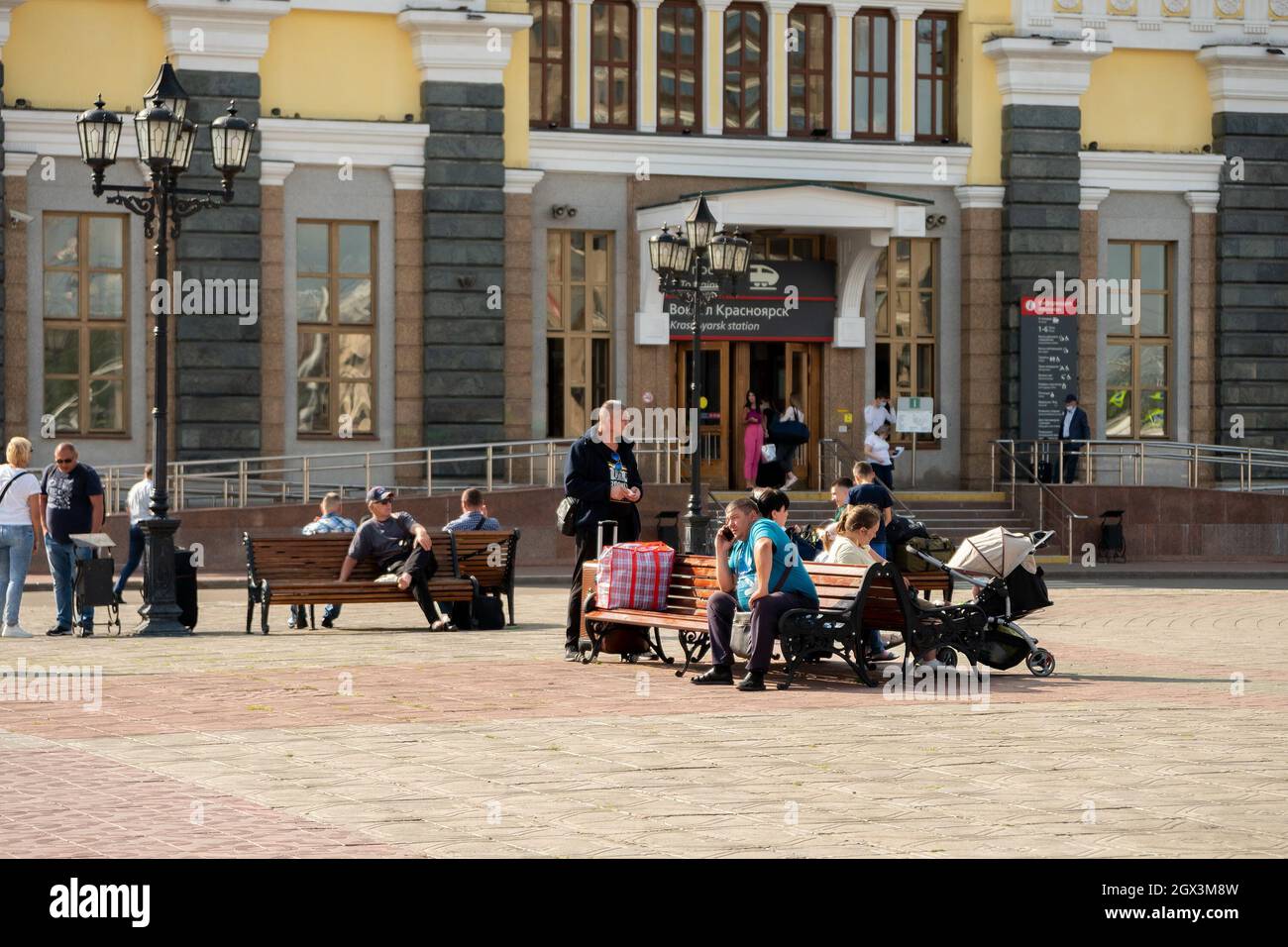 An einem sonnigen Sommertag sitzen Menschen auf Bänken auf dem Bahnhofsplatz vor dem Hintergrund des Eingangs zum Hauptbahnhof der Stadt Stockfoto