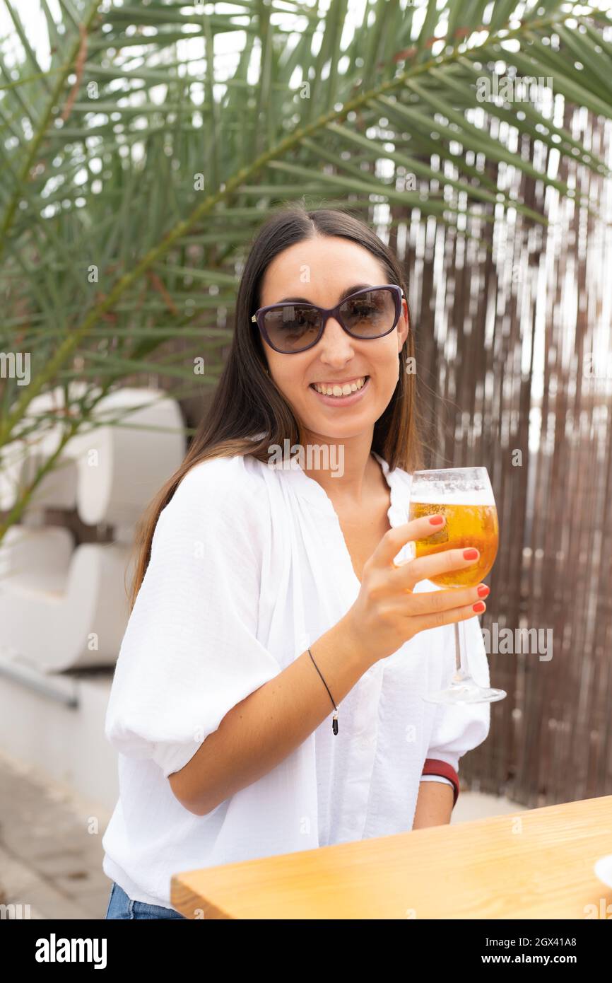 Nette junge Frau mit Sonnenbrille, die Bier auf einer Terrasse trinkt Stockfoto