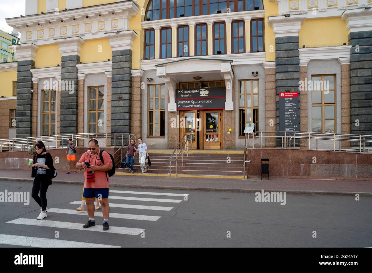 Die Menschen laufen am zentralen Eingang des Hauptbahnhofs der Stadt entlang der Fußgängerüberführung mit einer elektronischen Anzeigetafel auf Russisch. Stockfoto