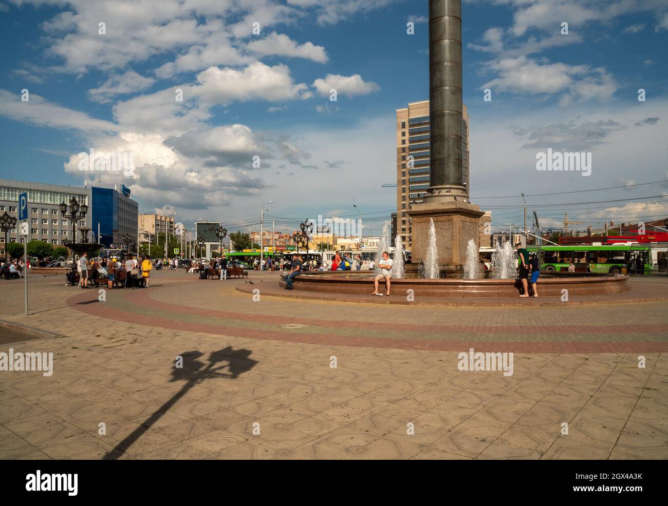 An einem sonnigen Sommertag ruhen sich die Menschen am Brunnen auf dem Bahnhofsplatz vor der Kulisse der Stadt in der Nähe des Hauptbahnhofs aus. Stockfoto